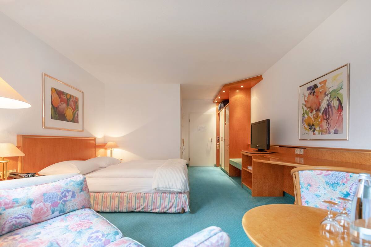 A hotel room with a bed, a sofa, a desk with a TV, and a chair.