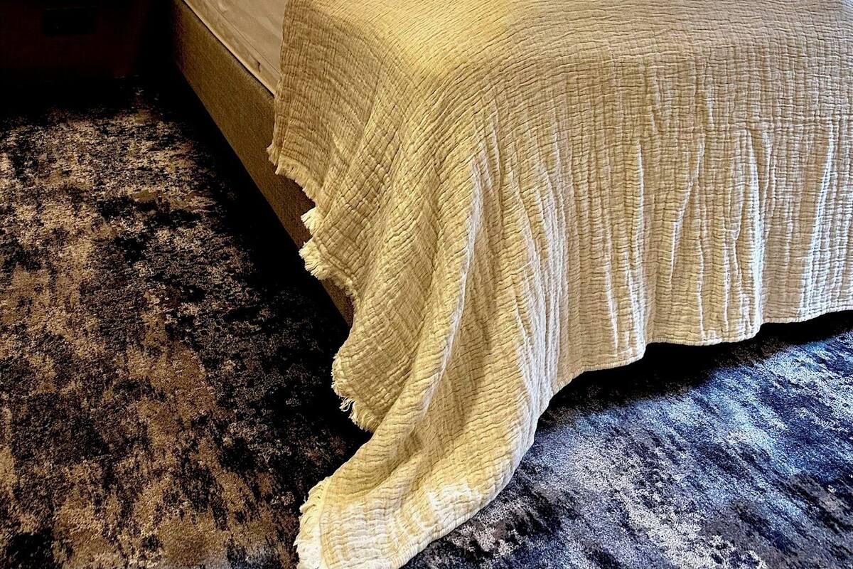 A hotel room with a large bed, striped wallpaper, two wall-mounted lamps, a nightstand, and a dark textured rug.