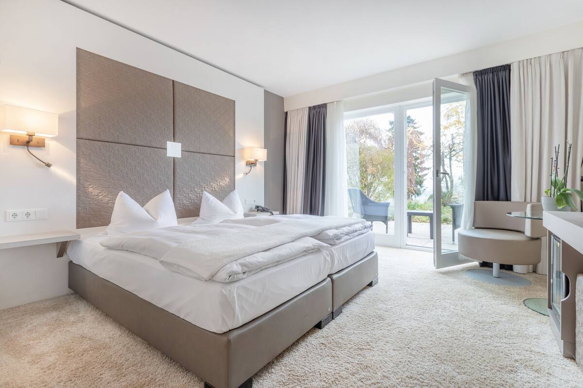 A modern hotel bedroom with a large bed, bedside lamps, a desk, and a view of the outdoors.