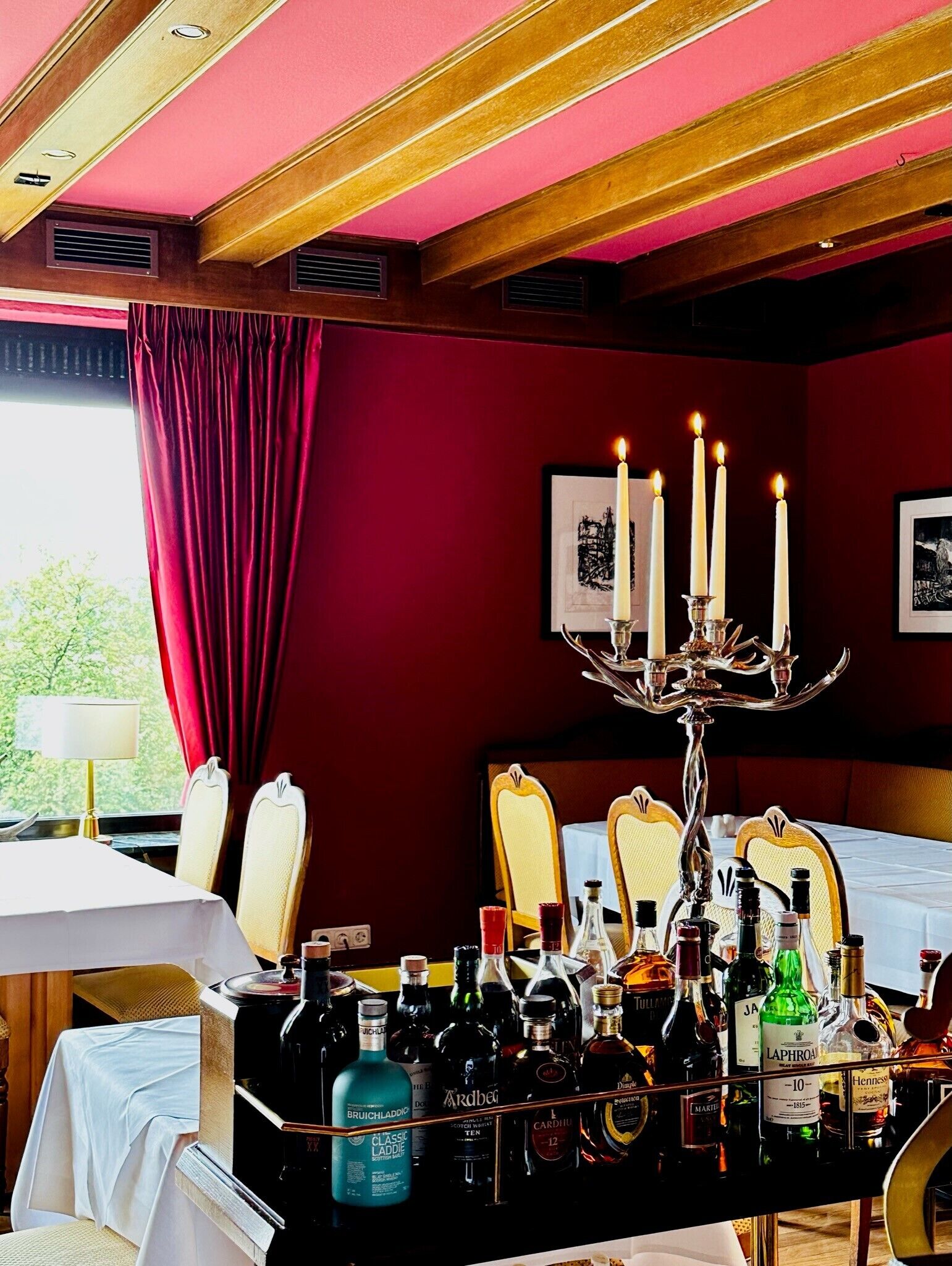 Una stanza con un tavolo apparecchiato per consumare i pasti, un candelabro con candele accese e diverse bottiglie di liquore.