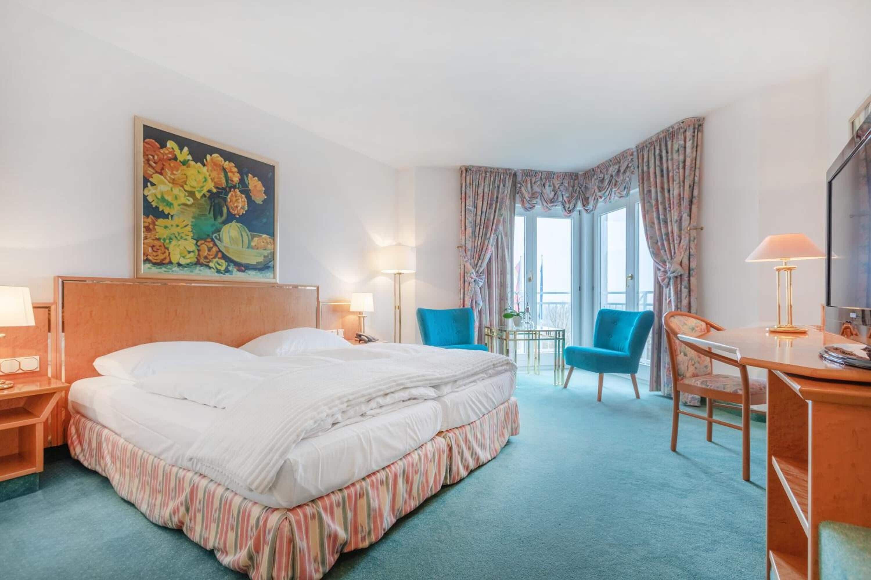 Habitación de hotel con una cama grande, un escritorio, dos sillas, una mesita y un cuadro en la pared.
