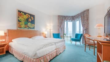 Habitación de hotel con una cama grande, un escritorio, dos sillas, una mesita y un cuadro en la pared.