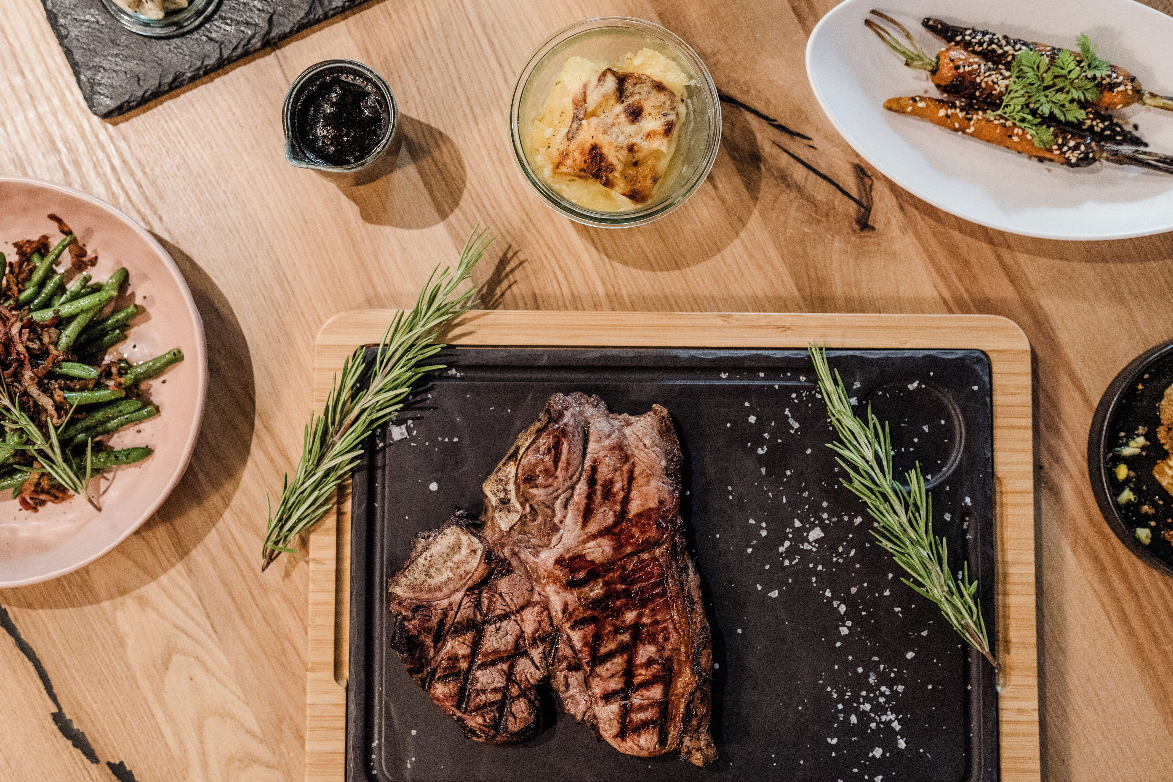 Una mesa de madera con diversos platos, incluyendo carne a la parrilla, verduras y un tazón de sopa.