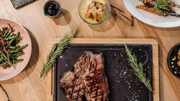 Una mesa de madera con diversos platos, incluyendo carne a la parrilla, verduras y un tazón de sopa.
