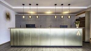 A modern reception desk with a metallic finish, overhead pendant lighting, and a decorative wall piece.
