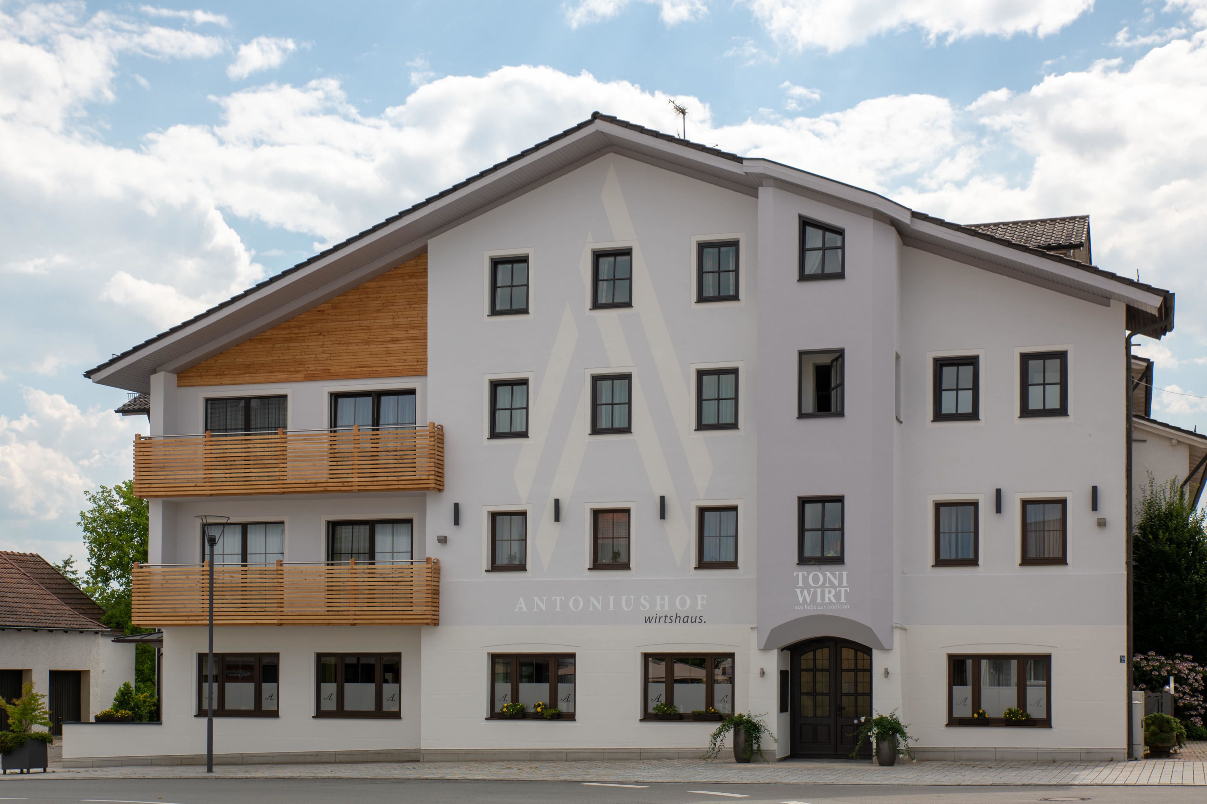 Ein mehrstöckiges Gebäude mit weißer Fassade, zahlreichen Fenstern und einem Holzbalkon.