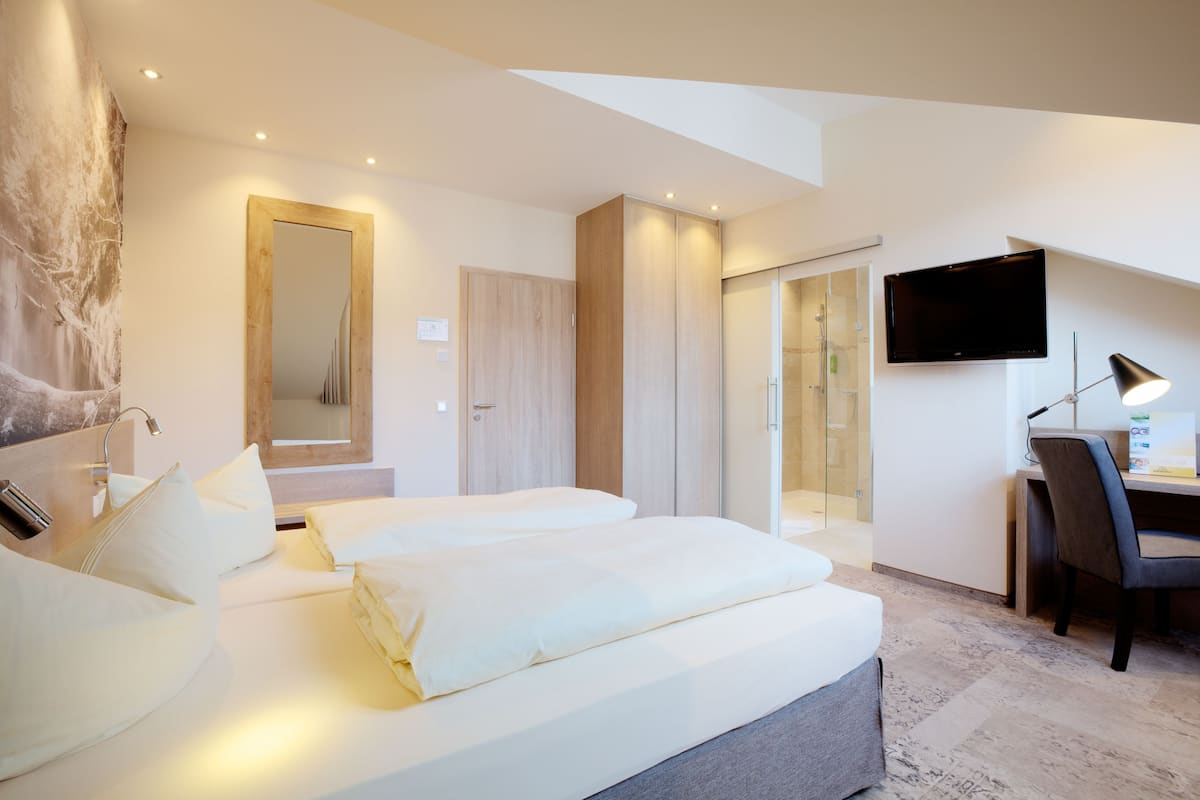 Una habitación de hotel moderna con dos camas, un escritorio, un televisor y zona de ducha.