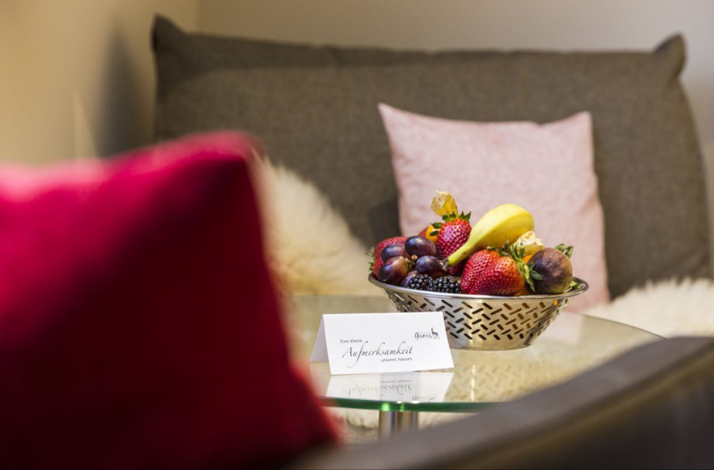 A bowl of fruit on a glass table with a card beside it.