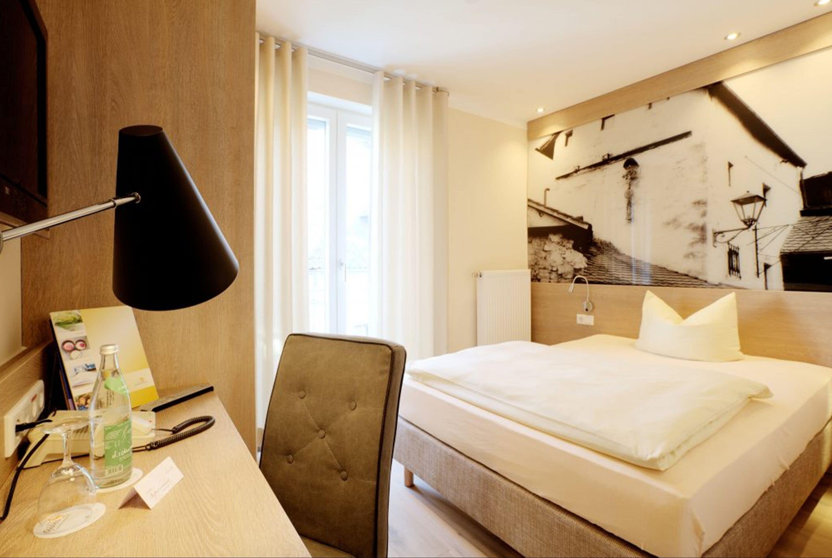 Une chambre d’hôtel comprenant un lit, un bureau avec une lampe, une chaise et une œuvre d’art accrochée au mur.