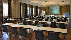 A conference room with long tables, black chairs, and a presentation screen. - Hotel Ratskeller (Salzgitter)