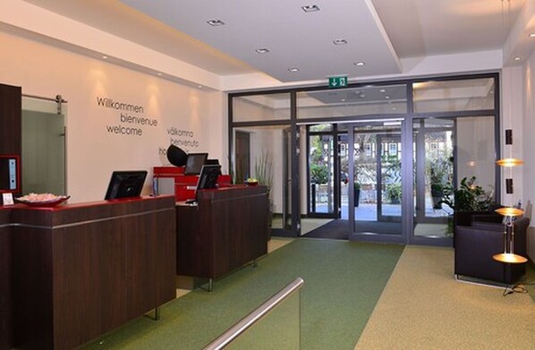 A reception area with a glass door entrance, a reception desk, and a wall with multilingual welcome signs.