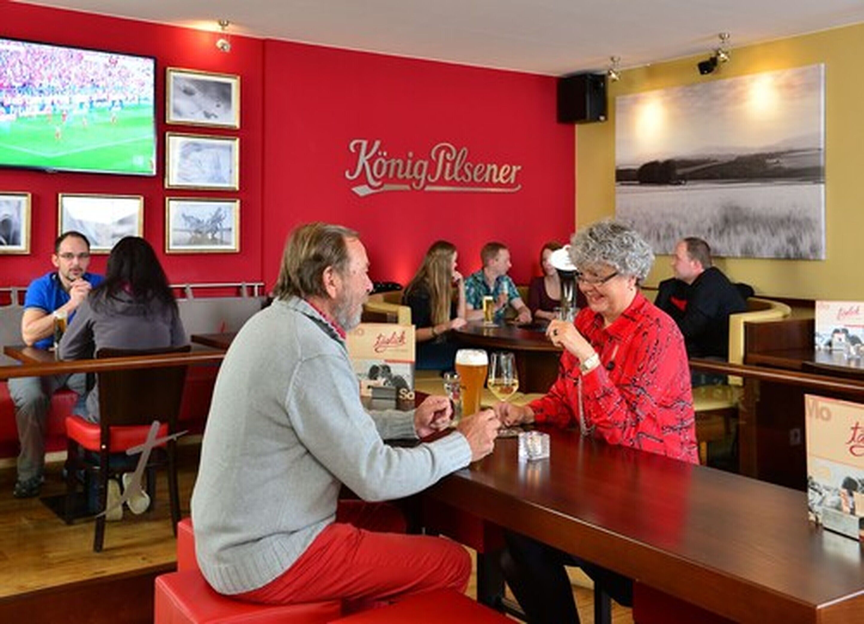 A bar with red walls and a large screen displaying a sports event.