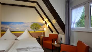 A hotel room with a sloped ceiling, two beds with white linens, an orange armchair, a small table with a vase, and a window with curtains.