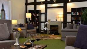 A modern living room with two sofas, a coffee table with wine glasses, bookshelves, and a fireplace. - Hotel Ratskeller (Salzgitter)