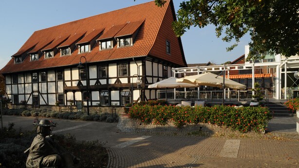 A traditional half-timbered building with a red-tiled roof, a paved courtyard, and outdoor seating area with umbrellas. - Hotel Ratskeller (Salzgitter)