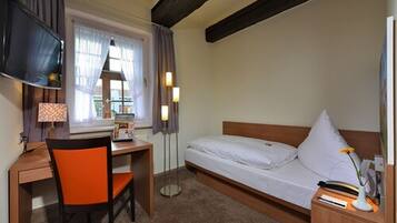 A hotel room with a bed, a desk, a chair, a TV, and a window with curtains.