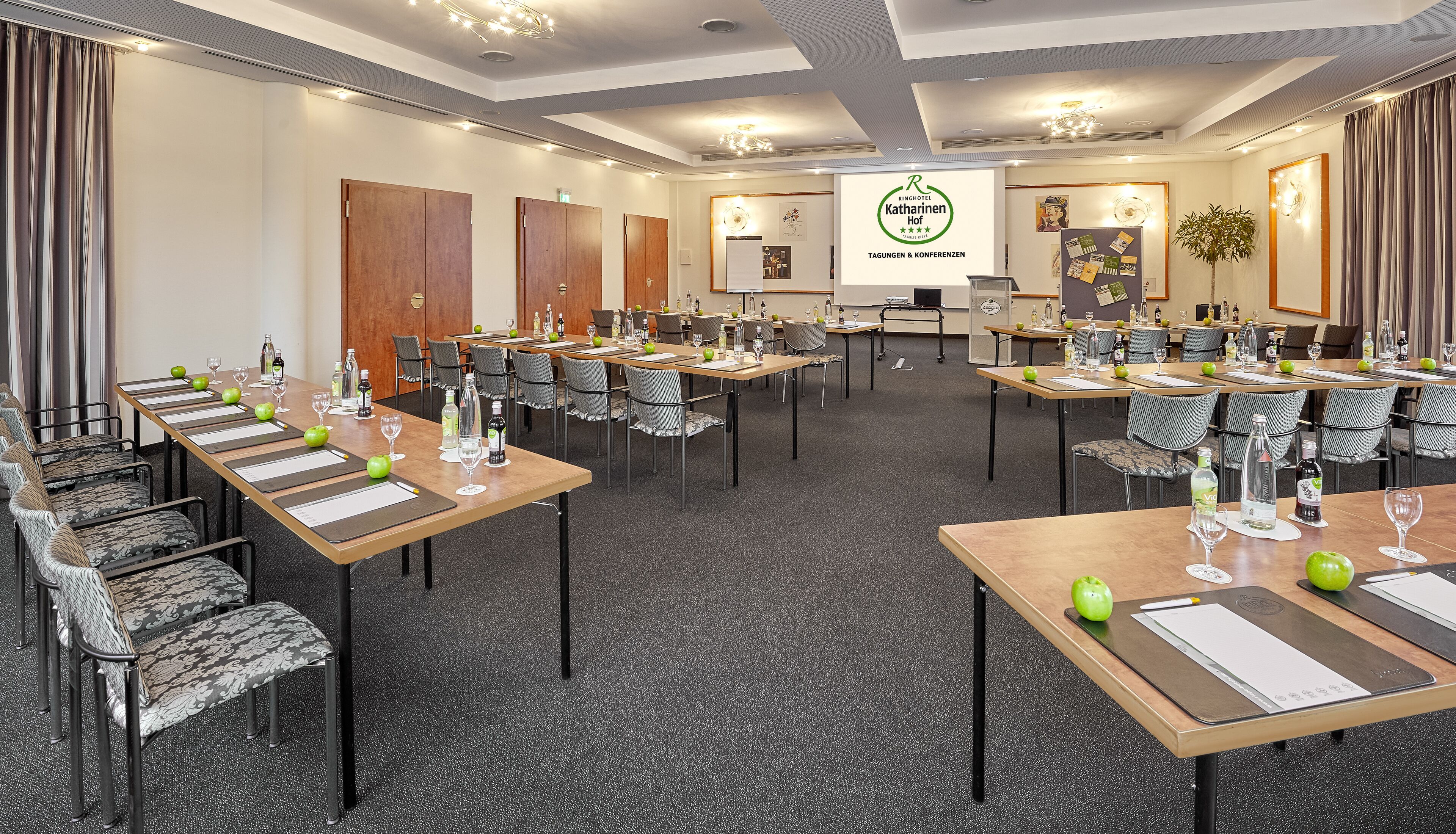 A conference room with multiple tables, chairs, and presentation screens.
