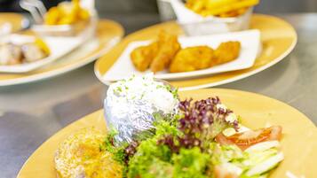A dining table with various dishes, including a salad with greens and a fish fillet, and a person serving food.