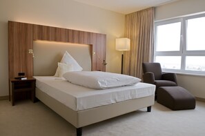 Ein Hotelzimmer mit einem großen Bett, einem Nachttisch, einem Sessel, einer Lampe und einem Fenster mit Vorhängen.