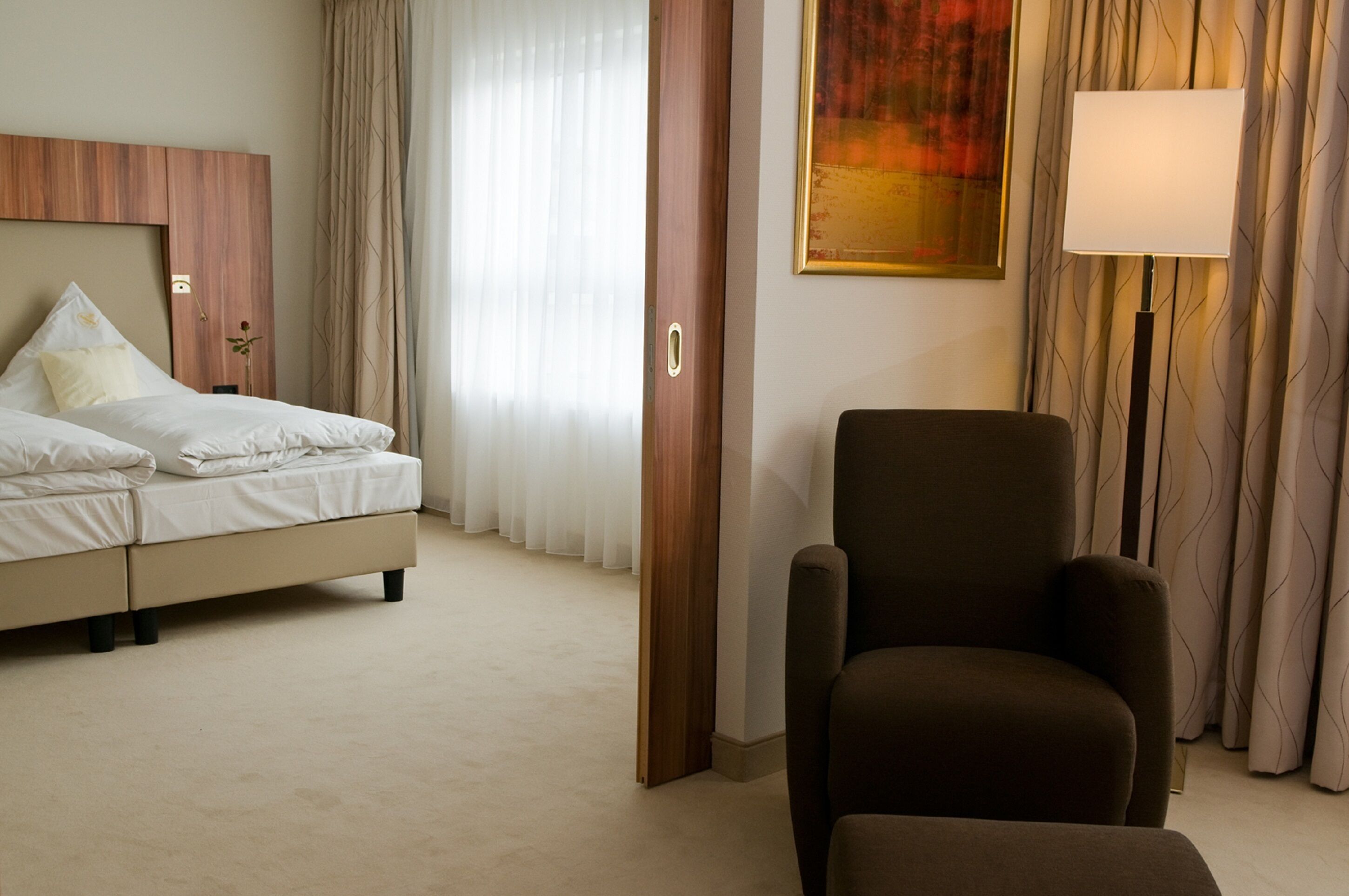 Ein Hotelzimmer mit Bett, Stuhl, Lampe und einem Bild an der Wand.