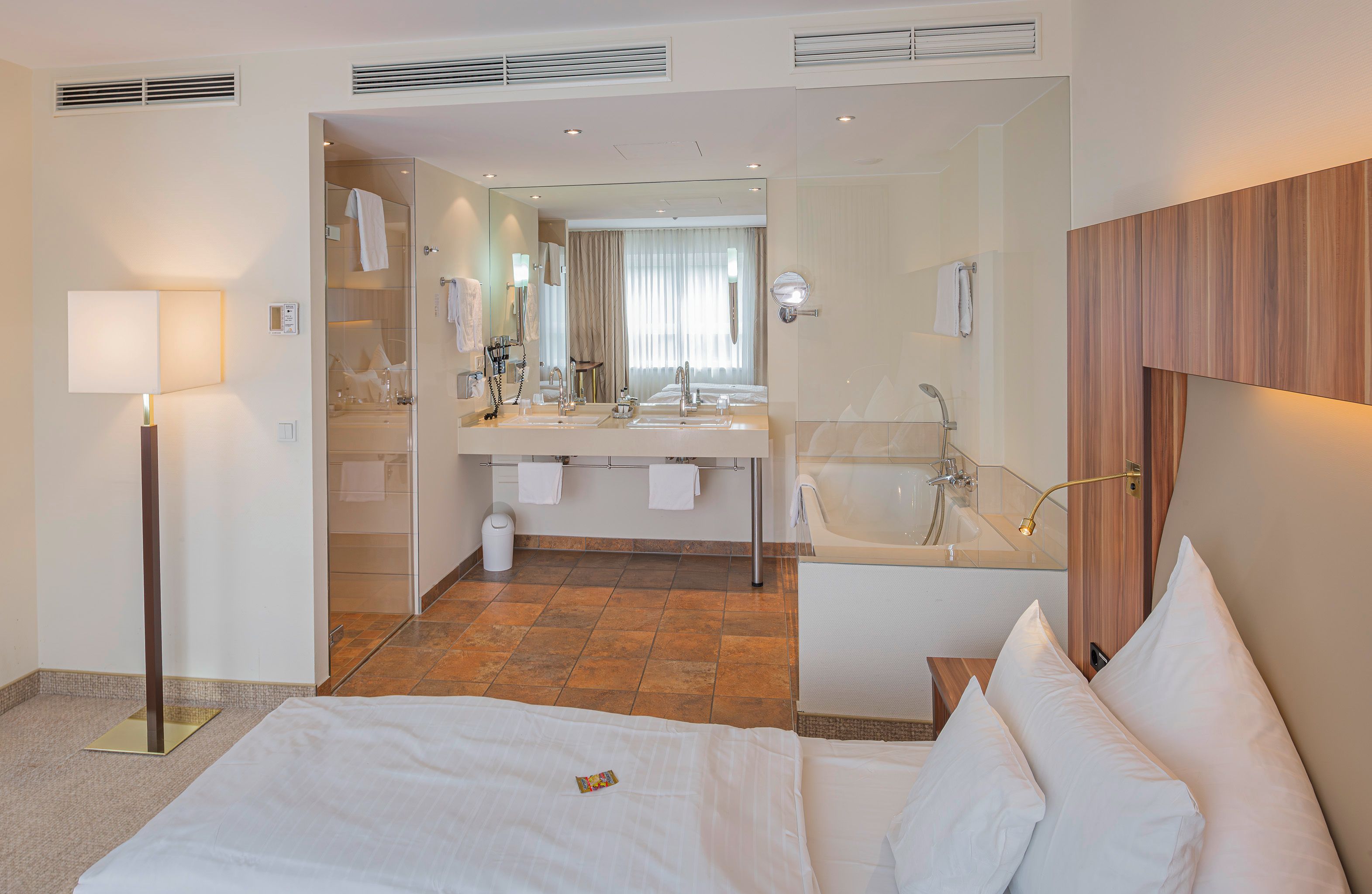 A hotel room with a bed, a sitting area, a bathroom with a bathtub, and a large mirror.