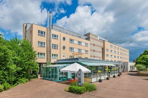 Un hotel con fachada moderna, un área de estar exterior cubierta y cielo despejado.