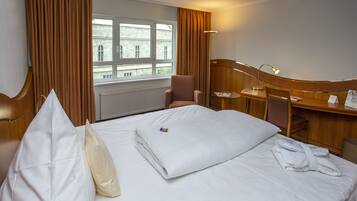 Ein Hotelzimmer mit Bett, Stuhl, Schreibtisch und einem Fenster mit Vorhängen.