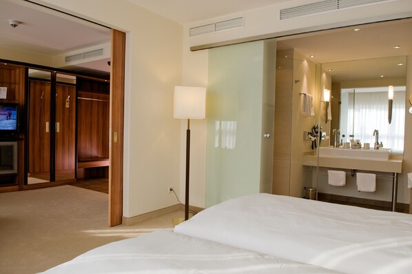 A hotel room with a large bed, a glass shower enclosure, a vanity with a mirror, and a television on the left wall. - Katharinenhof Hotelgesellschaft mbH & Co. KG (Unna)
