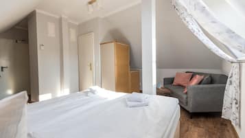 Een slaapkamer met een net opgemaakt bed, een grijze bank met kussens, een houten garderobe en een raam met een bloemenprint gordijn.