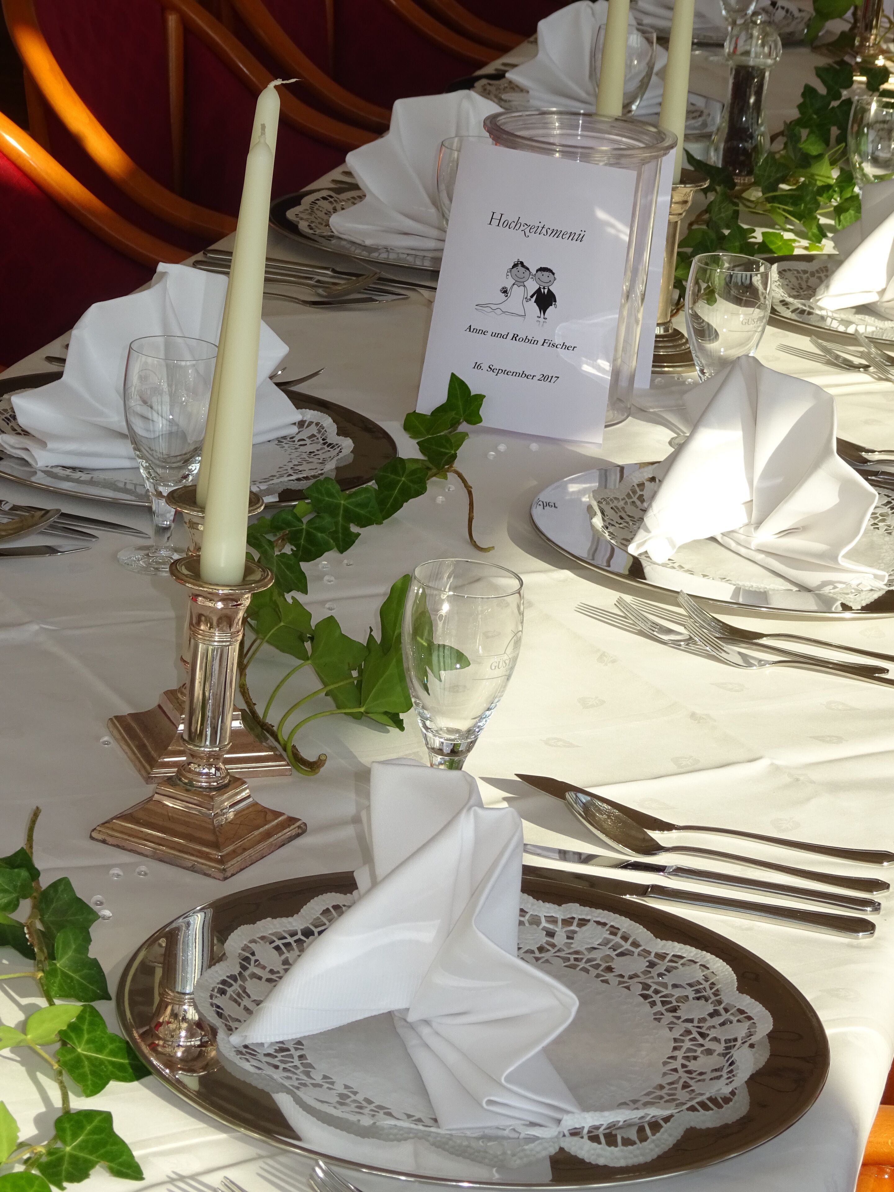 Une table dressée pour un événement formel, avec des nappes blanches, des couverts en argent et un menu.