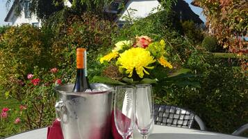 Eine Weinflasche in einem Eiskübel auf einem Tisch, zusammen mit zwei Gläsern, umgeben von Blumen und Grünpflanzen.