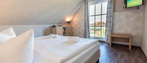 A hotel room with a large bed, a bedside table with a lamp, a TV mounted on the wall, and a window with curtains.