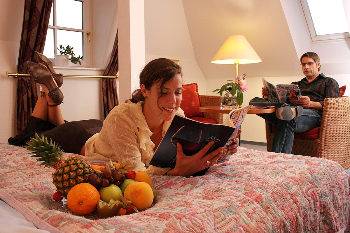 A hotel room with a bed, a window with curtains, a lamp, and a table with a plant.