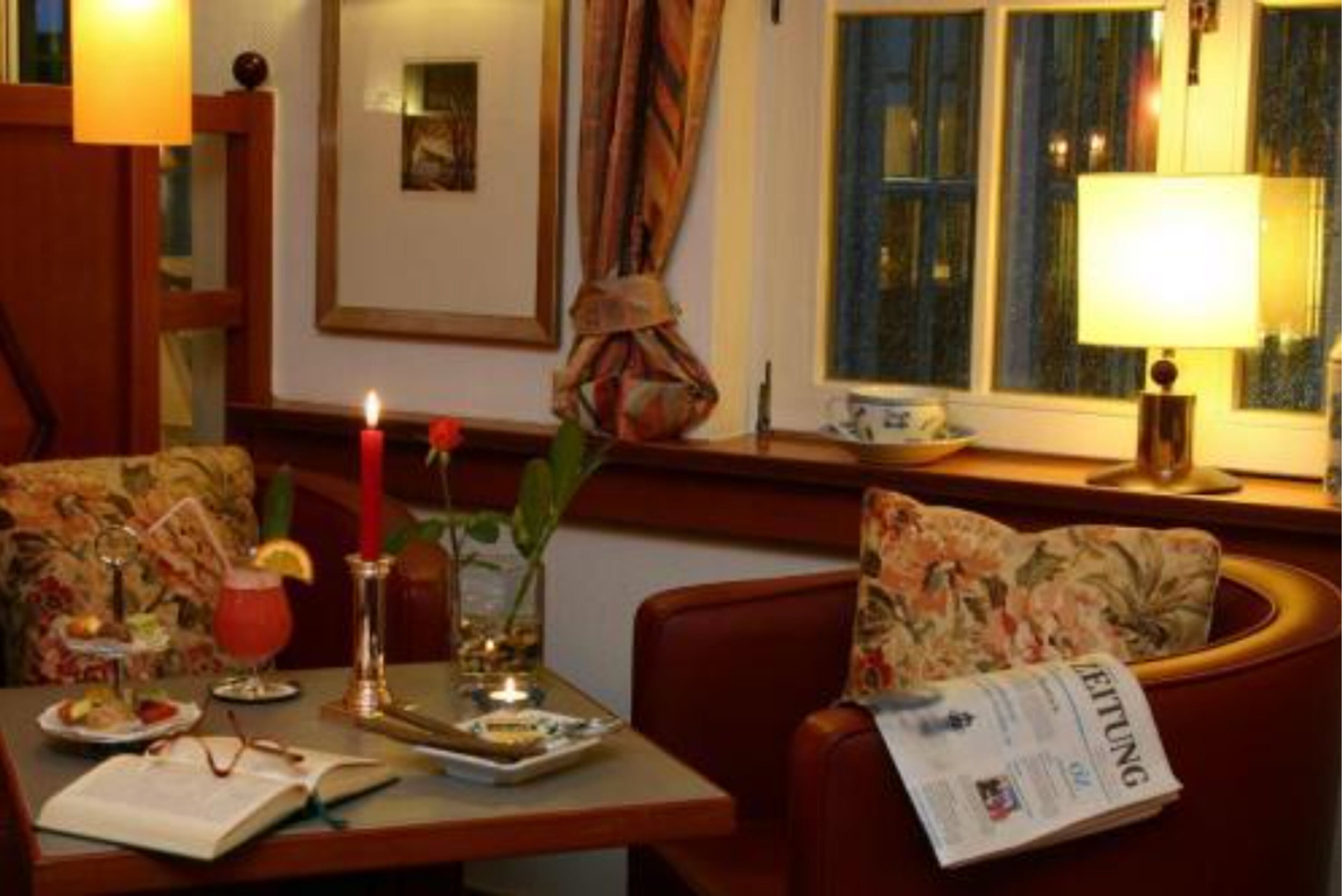 Una habitación acogedora con una mesa de comedor para dos, una vela, una bebida y un periódico.