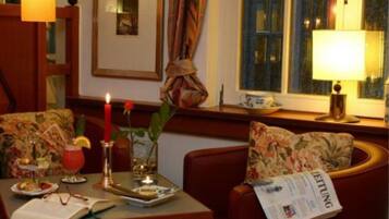 Una habitación acogedora con una mesa de comedor para dos, una vela, una bebida y un periódico.