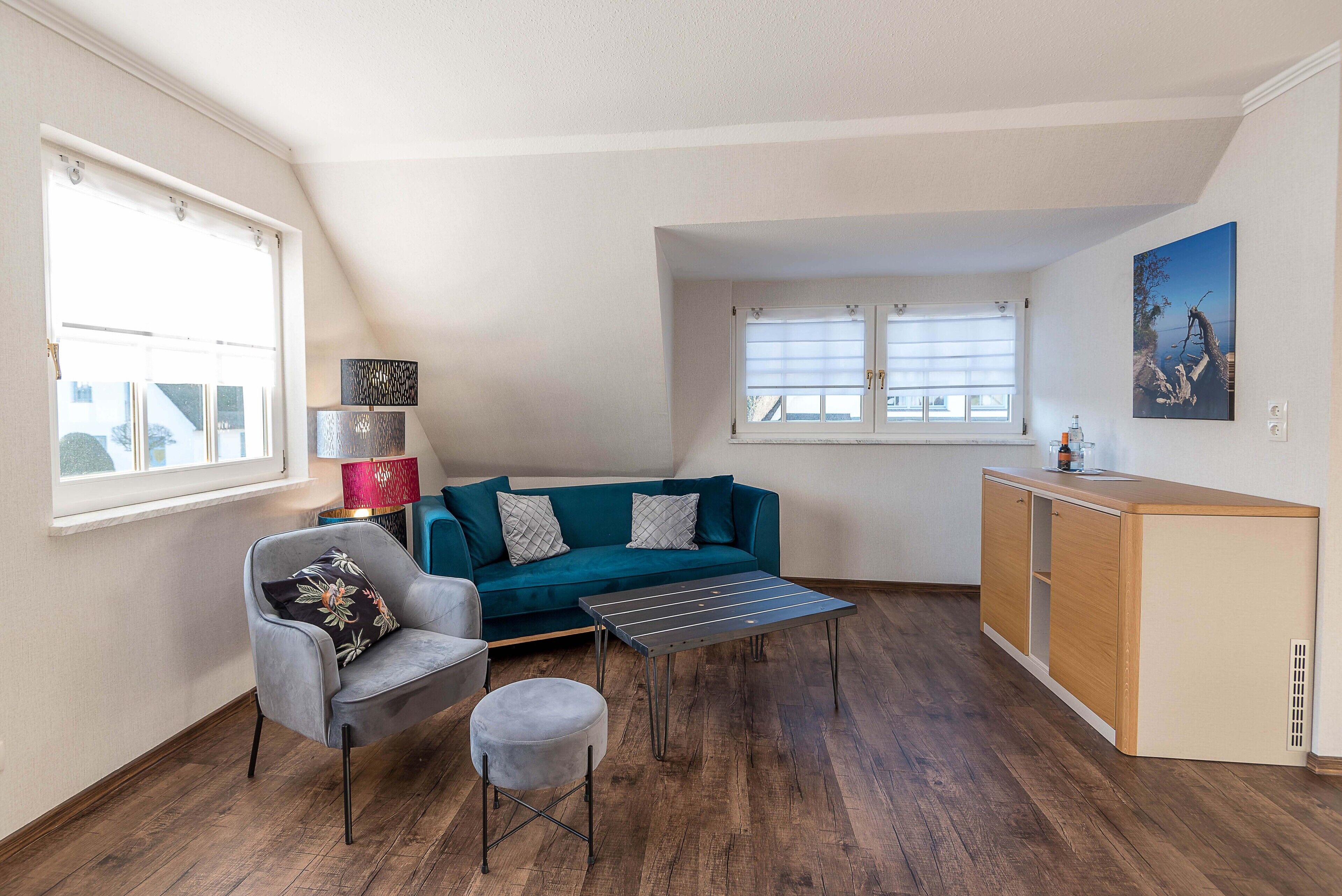 A compact living space with a sofa, a small table, a chair, and a kitchenette area.