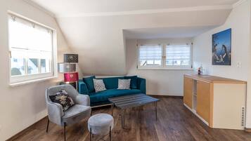 A compact living space with a sofa, a small table, a chair, and a kitchenette area.