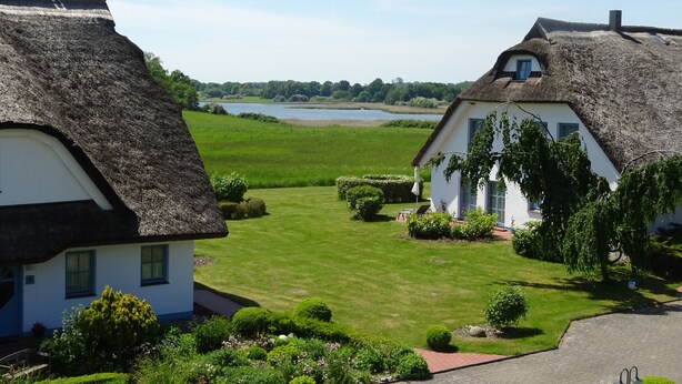 Two thatched-roof cottages with white walls, surrounded by well-maintained lawns and a lake in the background.