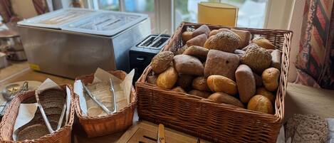 A breakfast buffet with various breads and pastries, a toaster, and a bread knife on a wooden counter.