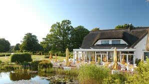 A lakeside hotel with outdoor seating, a pond, and lush greenery.