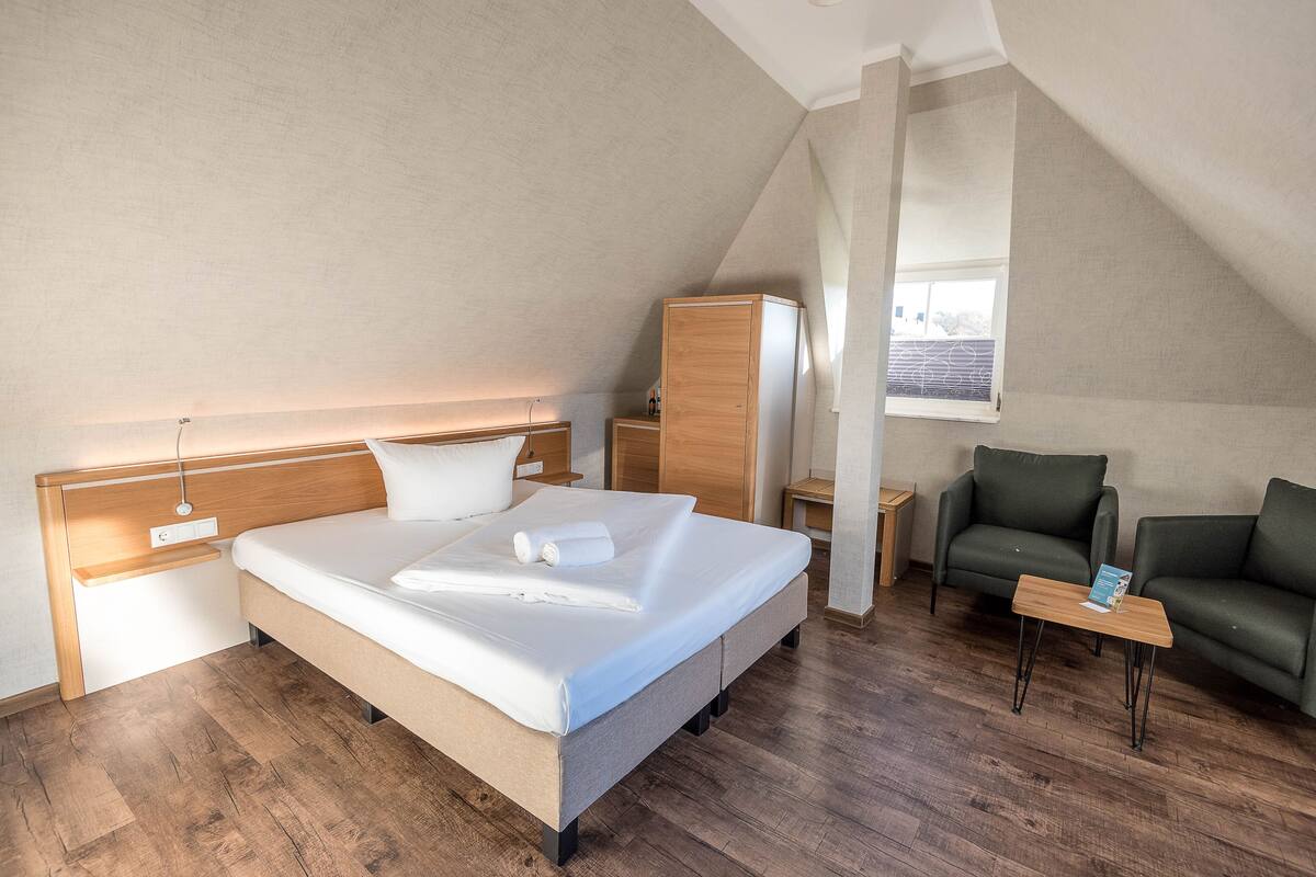 A modern hotel room with a large bed, a wooden headboard, a green sofa, a small wooden table, and a window with a view.