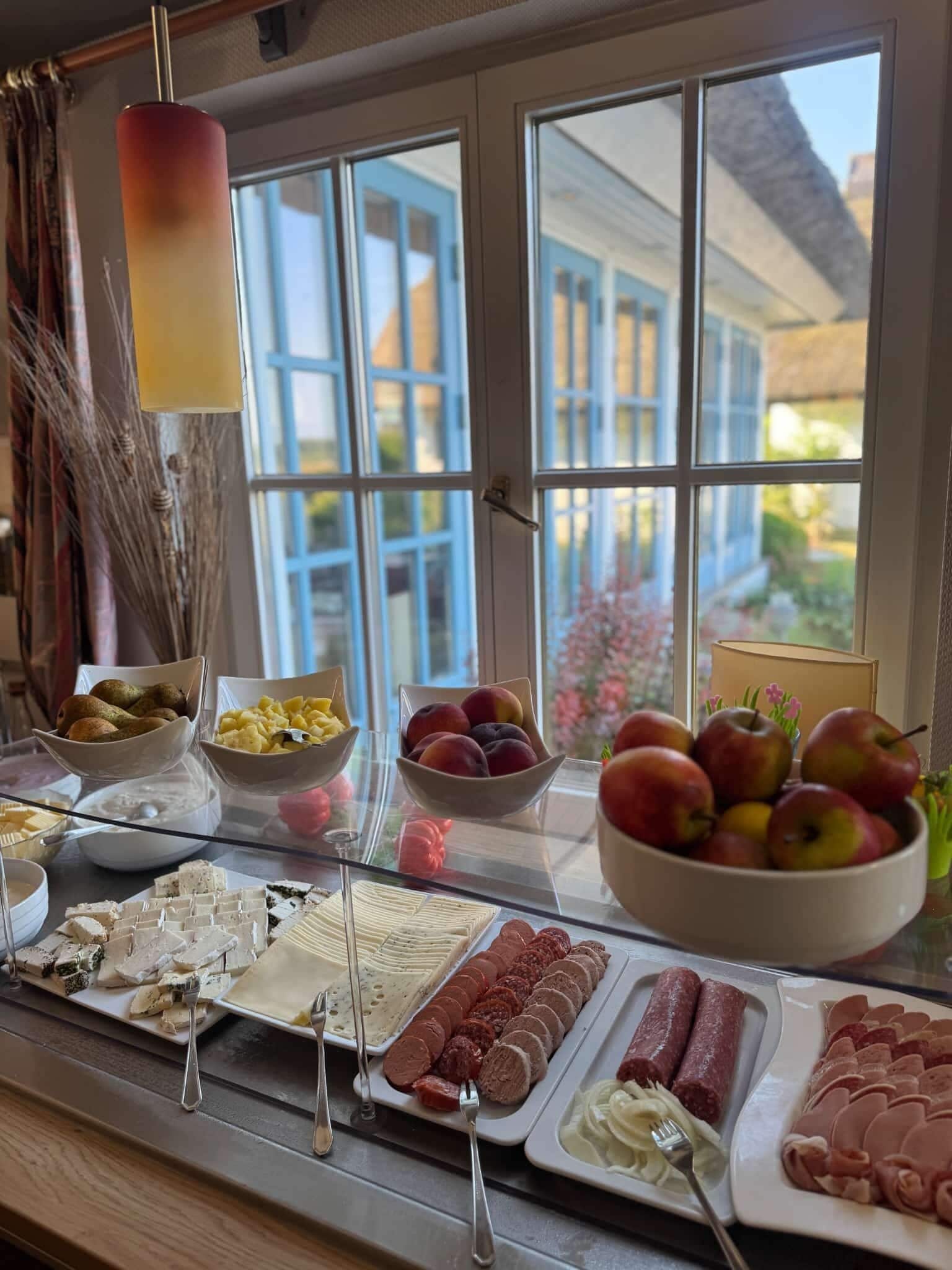 Una mesa de buffet con diversos alimentos y vistas a una casa a través de amplios ventanales.