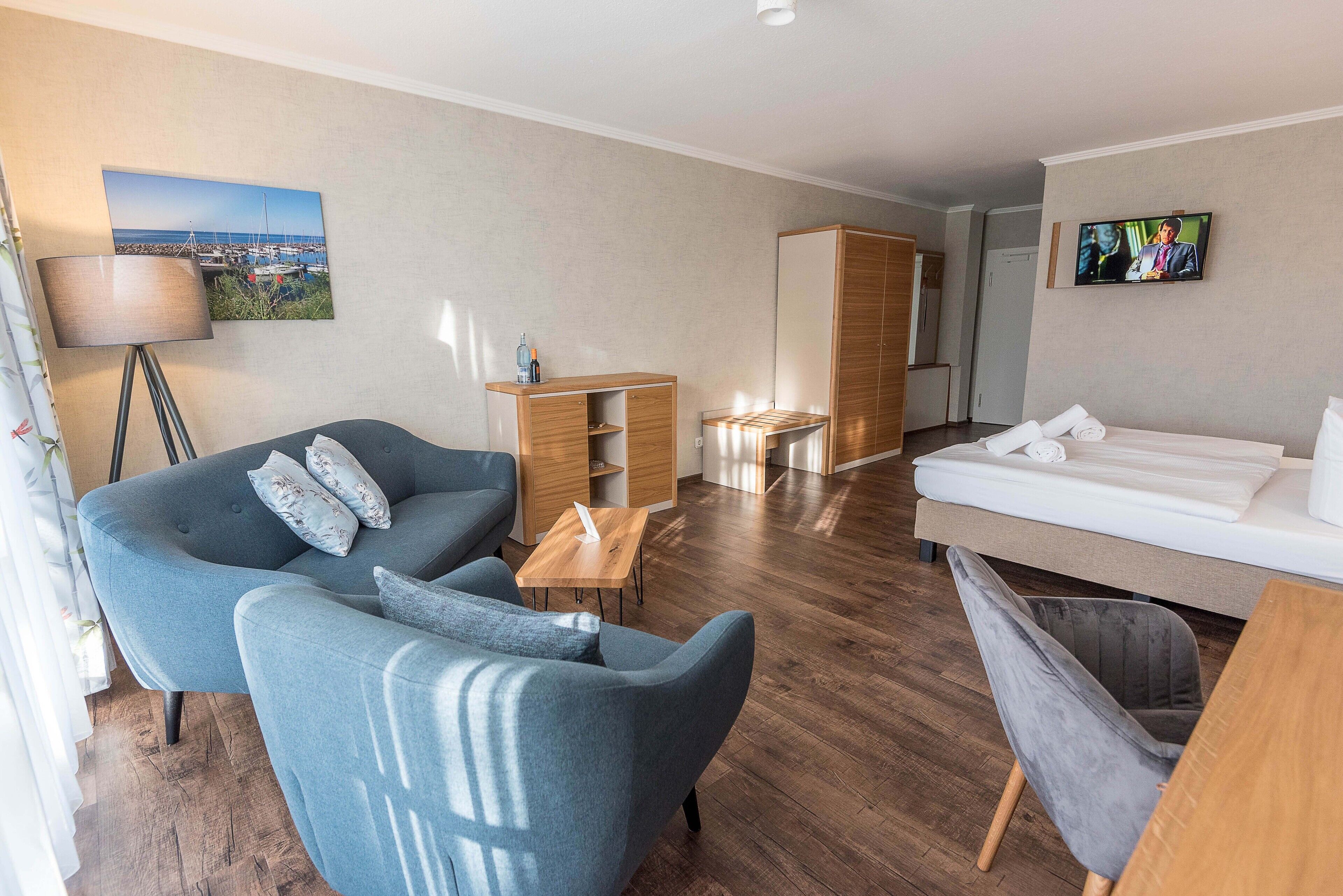 A modern hotel room with a sofa, a bed, a desk, and a TV.