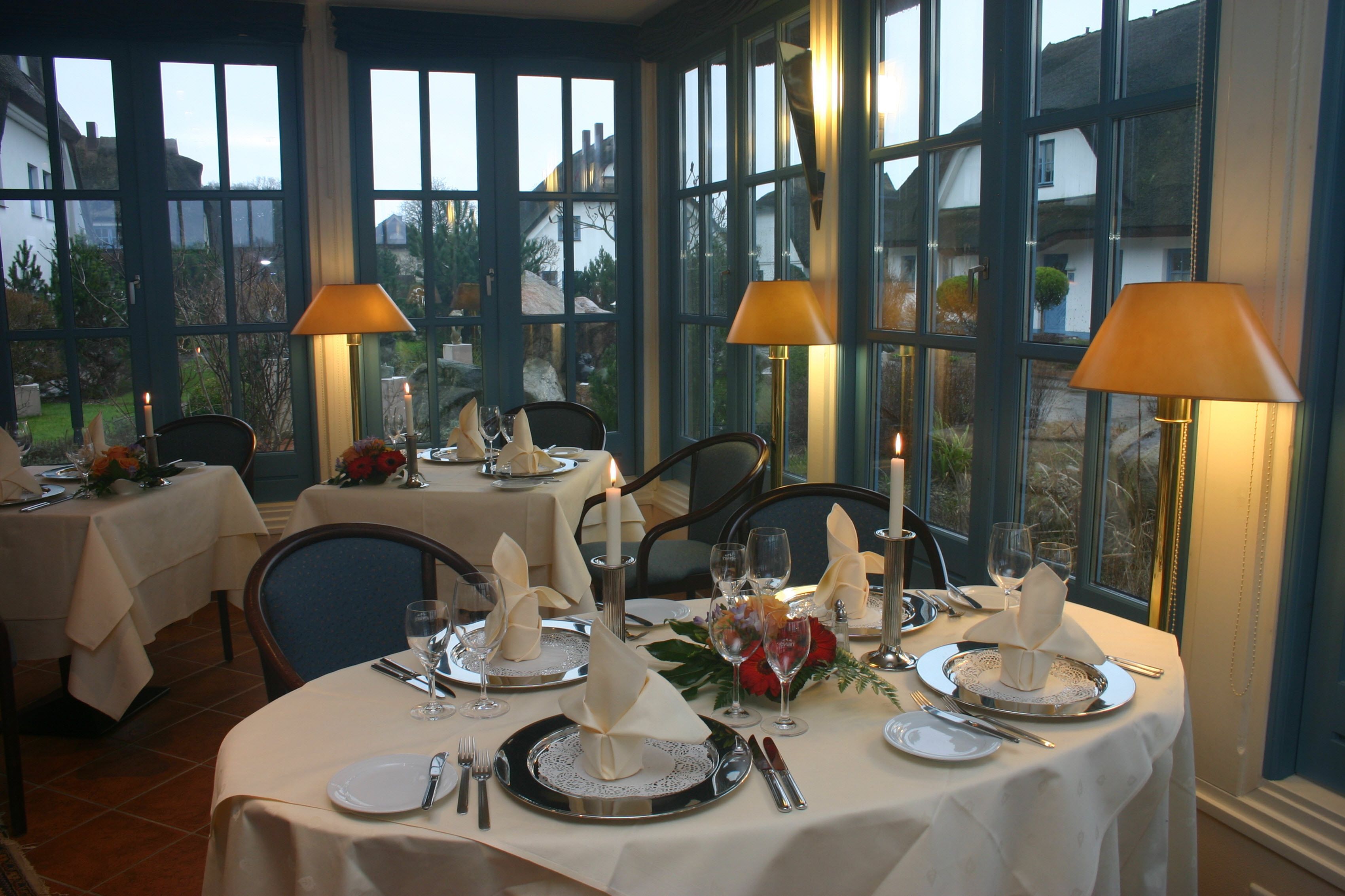 Un espace repas avec des tables rondes dressées pour le repas, chacune agrémentée d’une bougie, d’un arrangement floral et d’une nappe.