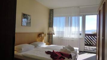 A hotel room with a bed, a nightstand, a lamp, a window with curtains, and a view of the outdoors.