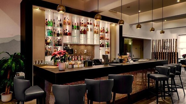 Een bar met een lange toonbank, meerdere flessenkasten en verschillende barkrukken.