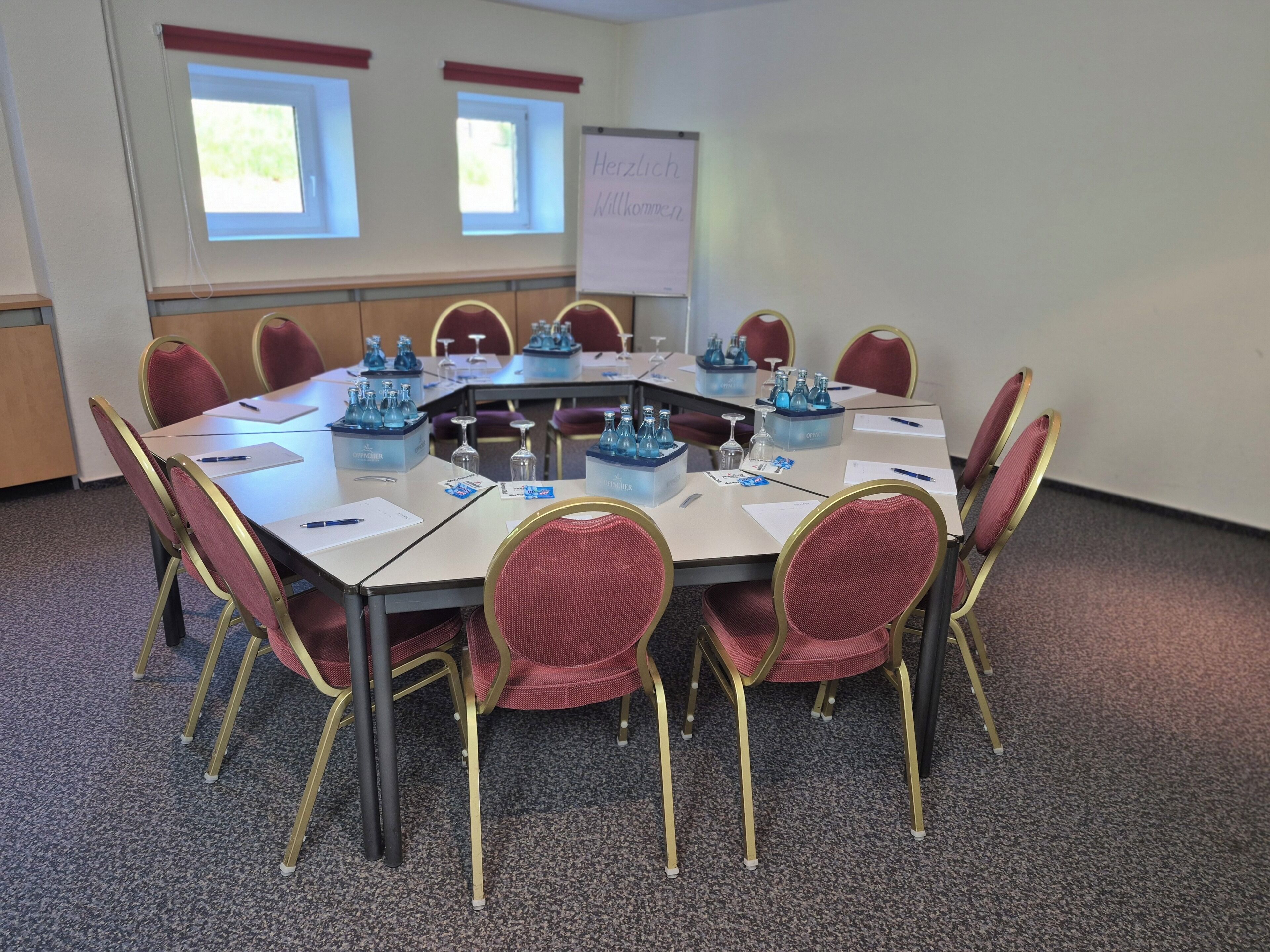 Ein Konferenzraum mit rundem Tisch, roten Stühlen und einer Whiteboard-Wand.