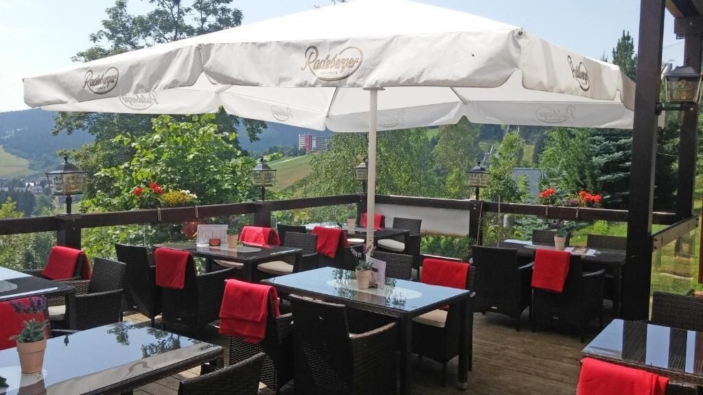 An outdoor patio area with tables and chairs, covered by white umbrellas, and a scenic view in the background.