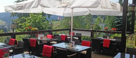 An outdoor patio area with tables and chairs, covered by white umbrellas, and a scenic view in the background.