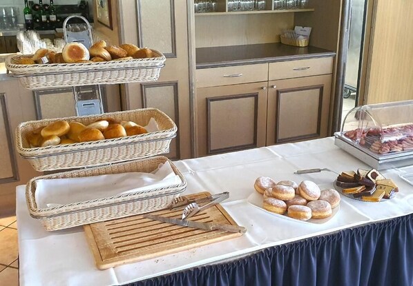 A buffet table with wicker baskets of bread, a cutting board, and a plate of pastries.